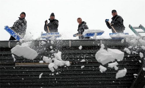 Hilfskräfte befreien ein Flachdach vom Schnee. Aufgrund der starken Schneefälle der vergangenen Wochen hatte ein Mitglied des Aschauer Gemeinderats angeregt, die Planungen für die neue Sporthalle hinsichtlich der Dachform zu überdenken. Foto dpa